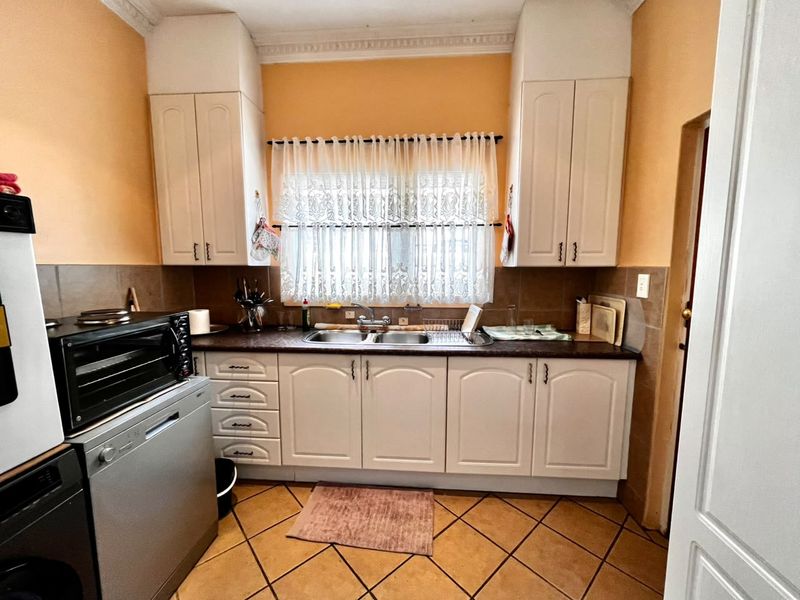 A functional kitchen featuring white built-in cabinetry, a double basin sink, tiled backsplash, and durable tiled flooring with classic crown molding details.