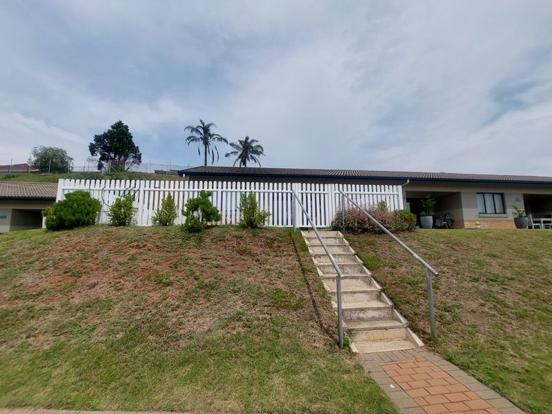 Front exterior view of the townhouse featuring a white picket fence, concrete staircase with metal handrails, and a brick paved walkway.