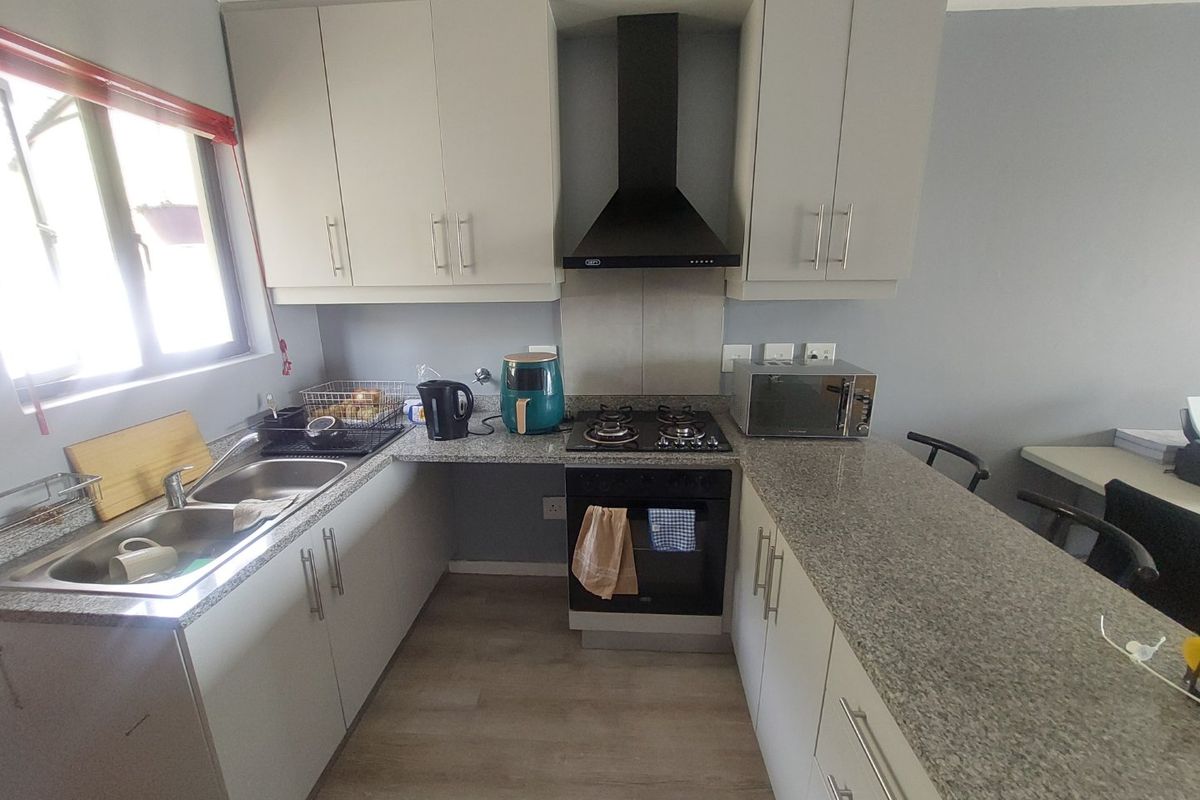 A functional kitchen featuring granite countertops, built-in cabinetry, a gas hob with extractor fan, and a double basin sink.