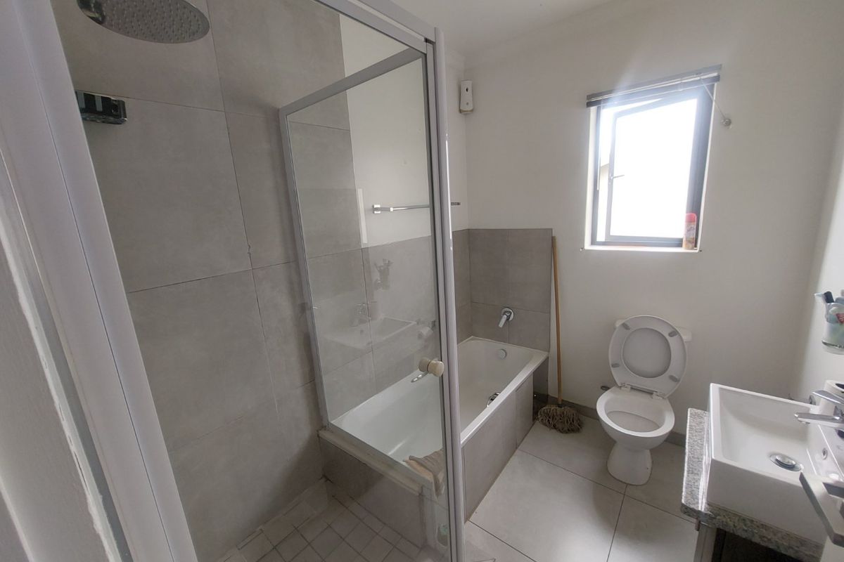 A functional bathroom featuring a separate shower enclosure, built-in bathtub, toilet, and a vanity basin with modern neutral wall and floor tiling.