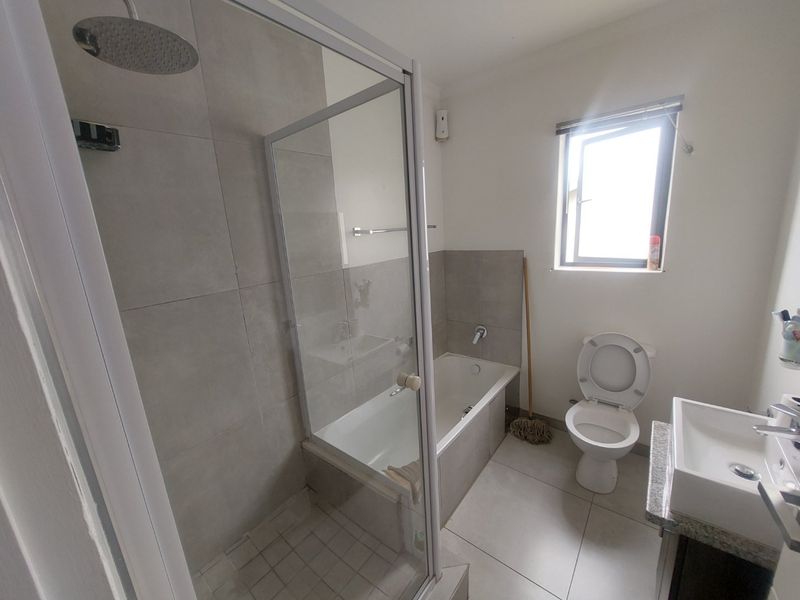 A functional bathroom featuring a separate shower enclosure, built-in bathtub, toilet, and a vanity basin with modern neutral wall and floor tiling.
