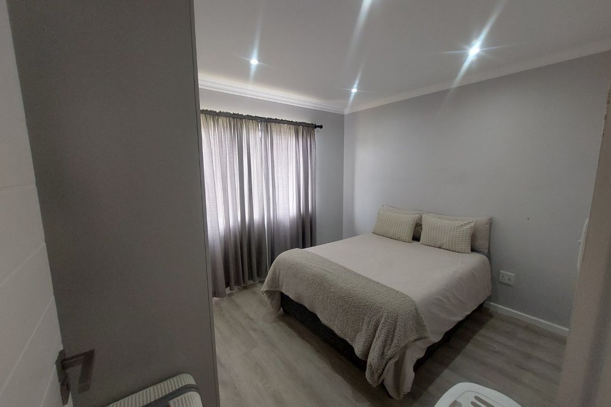 A well-maintained bedroom featuring neutral grey walls, modern laminate flooring, and recessed ceiling downlights.