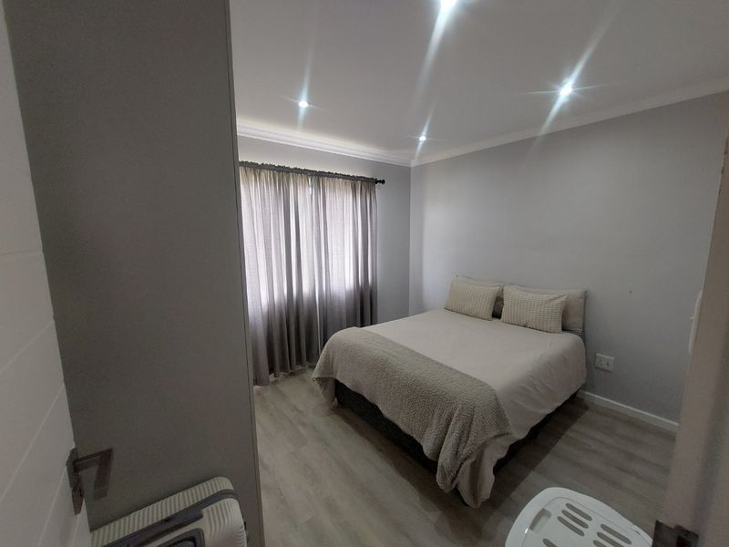 A well-maintained bedroom featuring neutral grey walls, modern laminate flooring, and recessed ceiling downlights.