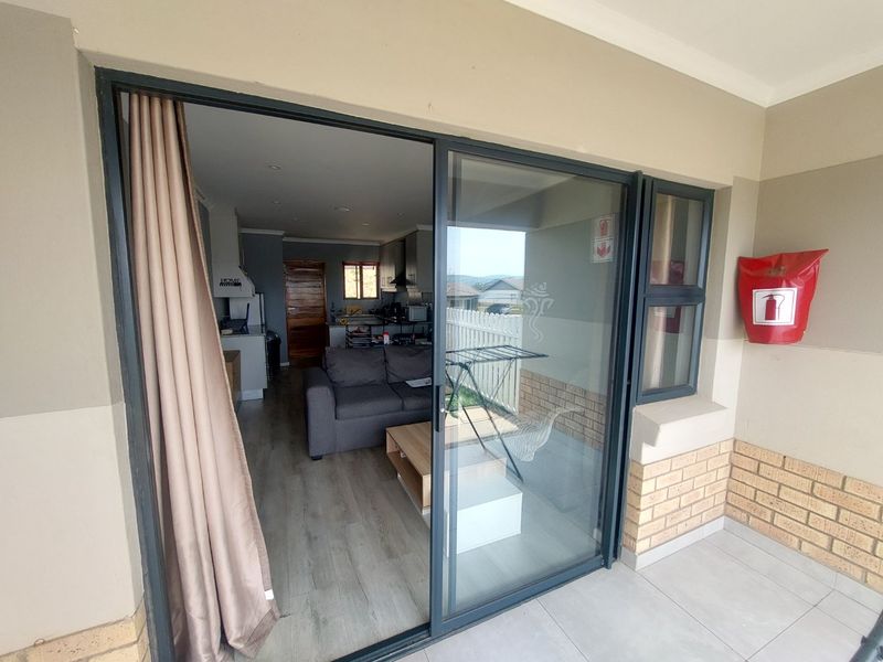 A covered patio area featuring tiled flooring, a brick base, and a sliding glass door providing access to the open-plan living and kitchen space.