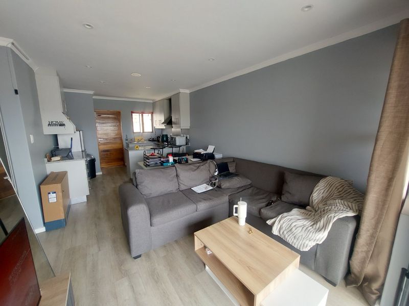 Open-plan living area featuring laminate flooring, recessed lighting, and a functional kitchen with built-in cabinetry and an extractor fan.