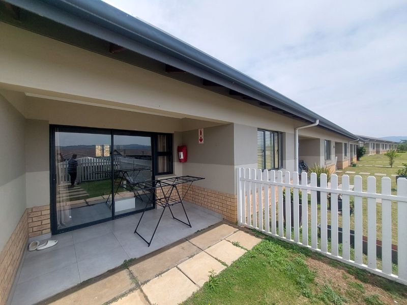 A covered patio area featuring tiled flooring, a sliding glass door entrance, and a white picket fence overlooking a shared garden space.