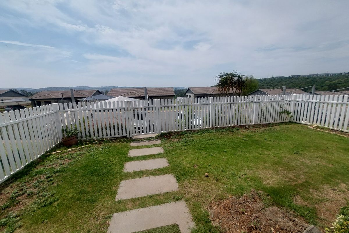 A private rear garden featuring a white picket fence, a paved walkway, and a lawn area with views of the surrounding residential estate.