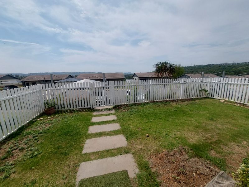 A private rear garden featuring a white picket fence, a paved walkway, and a lawn area with views of the surrounding residential estate.