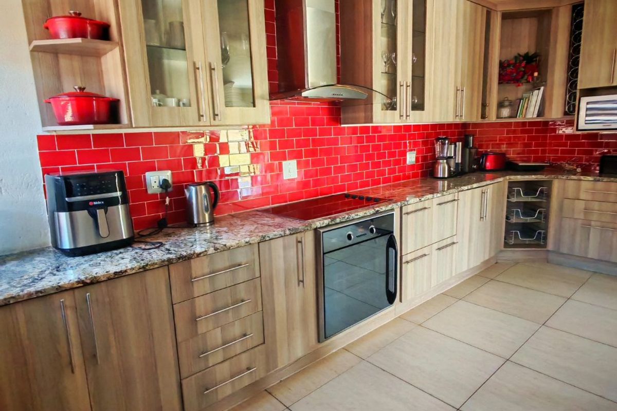 A well-maintained kitchen featuring light wood cabinetry, granite countertops, a vibrant red subway tile backsplash, and integrated stainless steel appliances.