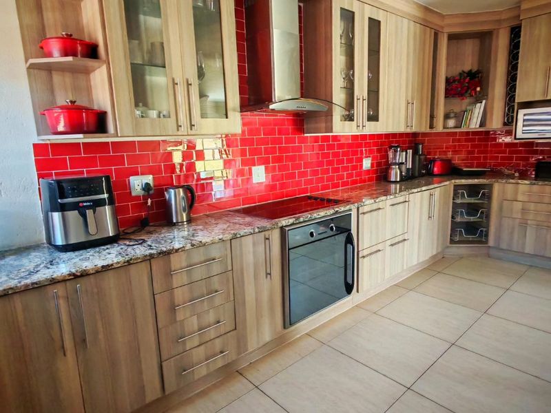 A well-maintained kitchen featuring light wood cabinetry, granite countertops, a vibrant red subway tile backsplash, and integrated stainless steel appliances.