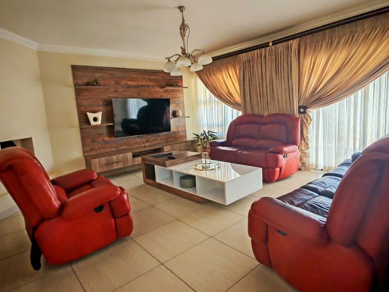 Spacious living room featuring tiled flooring, a built-in media unit, and large windows with curtain tracks.