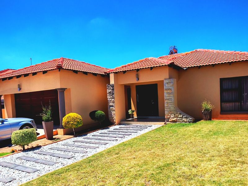 A well-maintained single-story home featuring a tiled roof, stone-clad entrance pillars, and a paved walkway leading to the front door.