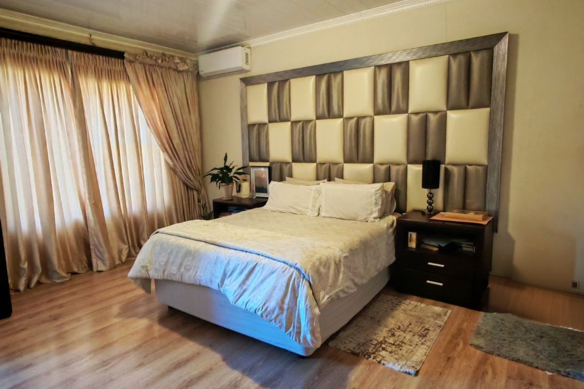 Spacious bedroom featuring laminate flooring, a wall-mounted air conditioning unit, and a decorative headboard wall panel.