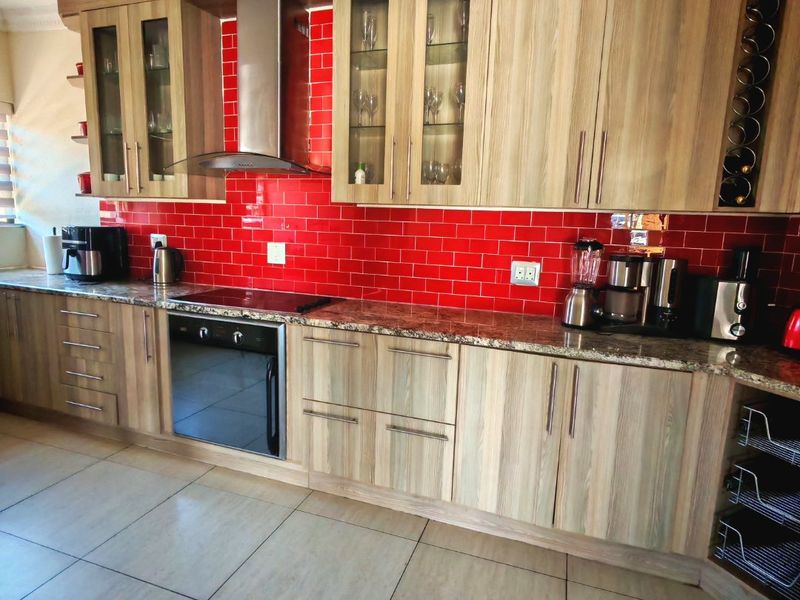 A well-maintained kitchen featuring wood-finish cabinetry, granite countertops, a vibrant red subway tile backsplash, and integrated stainless steel appliances.
