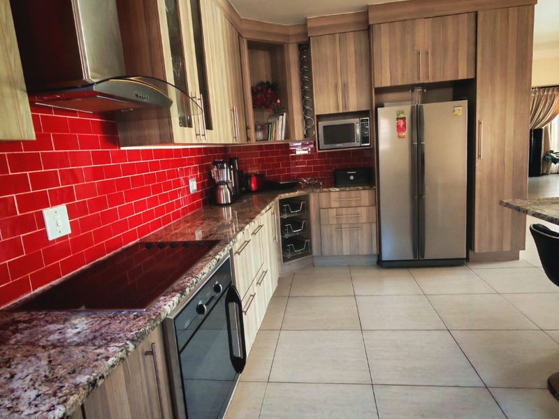A functional kitchen featuring wood-finish cabinetry, granite countertops, a bold red subway tile backsplash, and integrated appliances including an oven and hob.