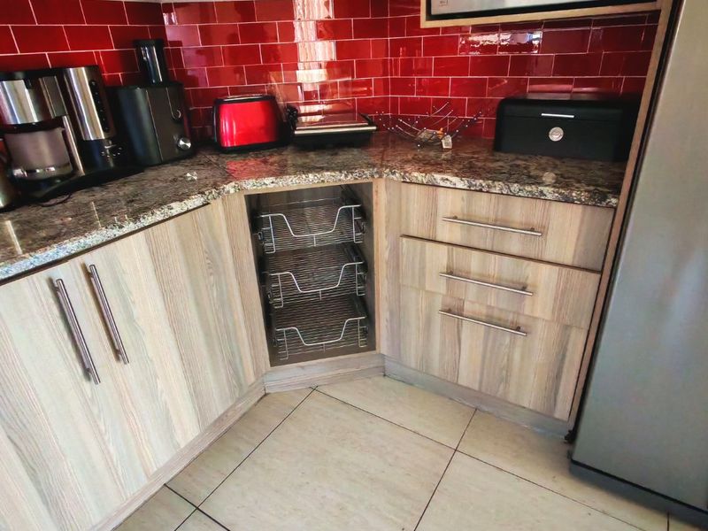 A functional kitchen corner featuring granite countertops, wood-look laminate cabinetry, pull-out wire storage drawers, and a vibrant red tiled backsplash.
