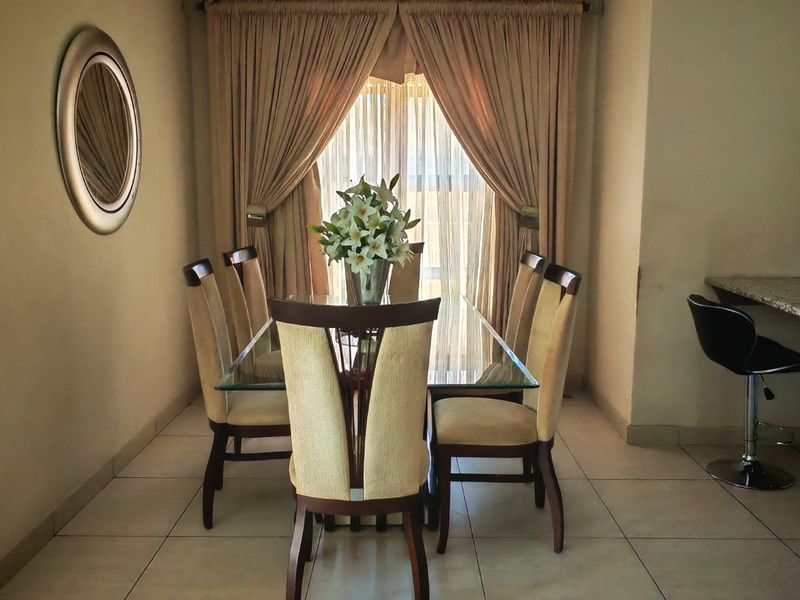 A well-lit dining area featuring neutral tiled flooring, crown molding, and an adjacent granite breakfast bar, creating a functional and cohesive living space.