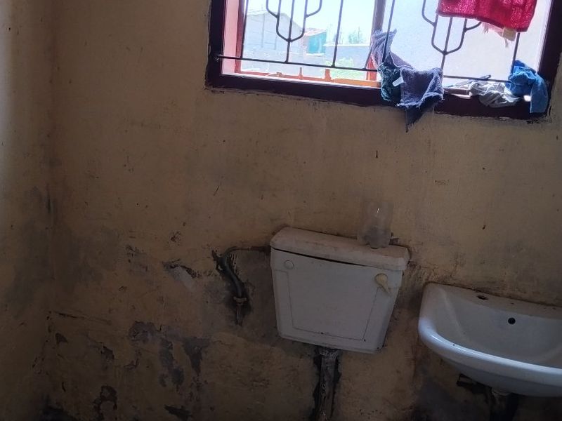 A small bathroom featuring a basic toilet and washbasin, requiring significant wall repairs and cosmetic updates to improve the overall condition.