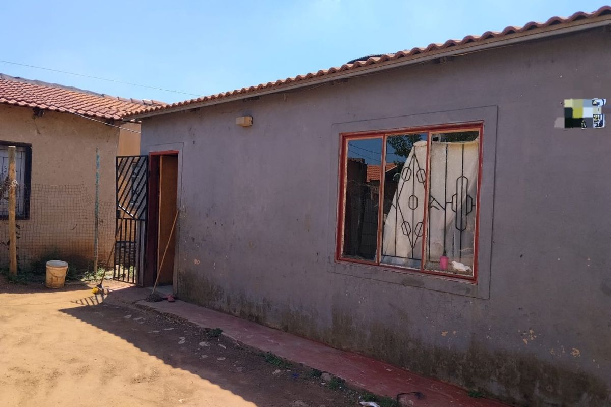 Rear exterior view of a single-story house featuring terracotta roof tiles, security gate, and metal-framed windows with burglar bars.