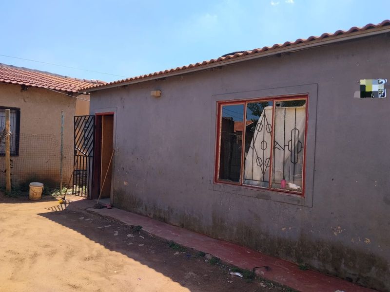 Rear exterior view of a single-story house featuring terracotta roof tiles, security gate, and metal-framed windows with burglar bars.