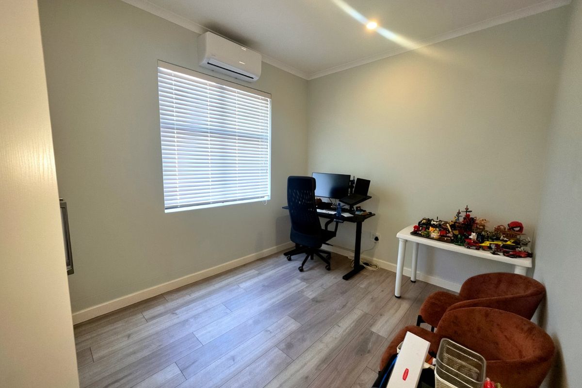 A well-maintained bedroom featuring modern laminate flooring, a split-system air conditioner, and venetian blinds, offering a clean and functional space.