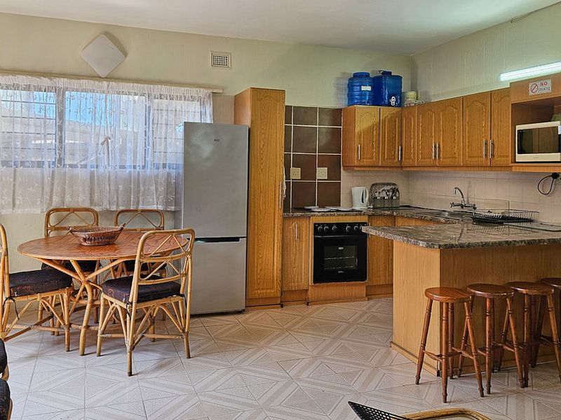 Open-plan kitchen and dining area featuring wooden cabinetry, granite countertops, built-in oven, and a breakfast bar with tiled flooring throughout.