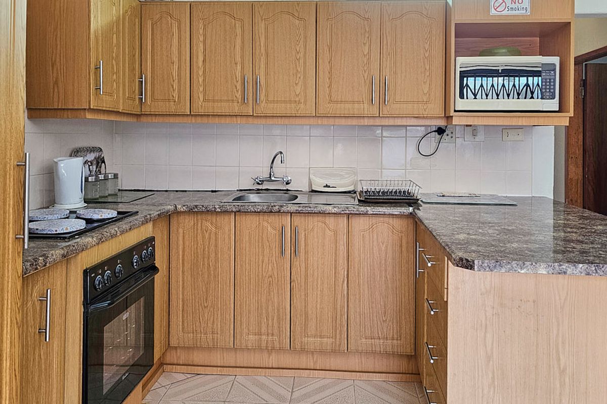 A functional kitchen featuring wood-look laminate cabinetry, granite-style countertops, a built-in oven, and a tiled backsplash, offering a practical layout for daily use.