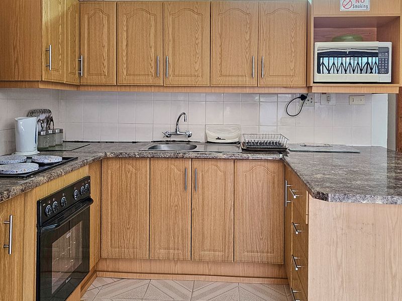 A functional kitchen featuring wood-look laminate cabinetry, granite-style countertops, a built-in oven, and a tiled backsplash, offering a practical layout for daily use.
