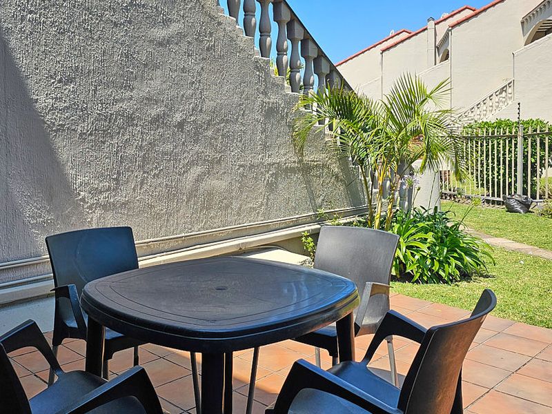 A private outdoor patio area featuring tiled flooring and a concrete balustrade, adjacent to a small garden space.