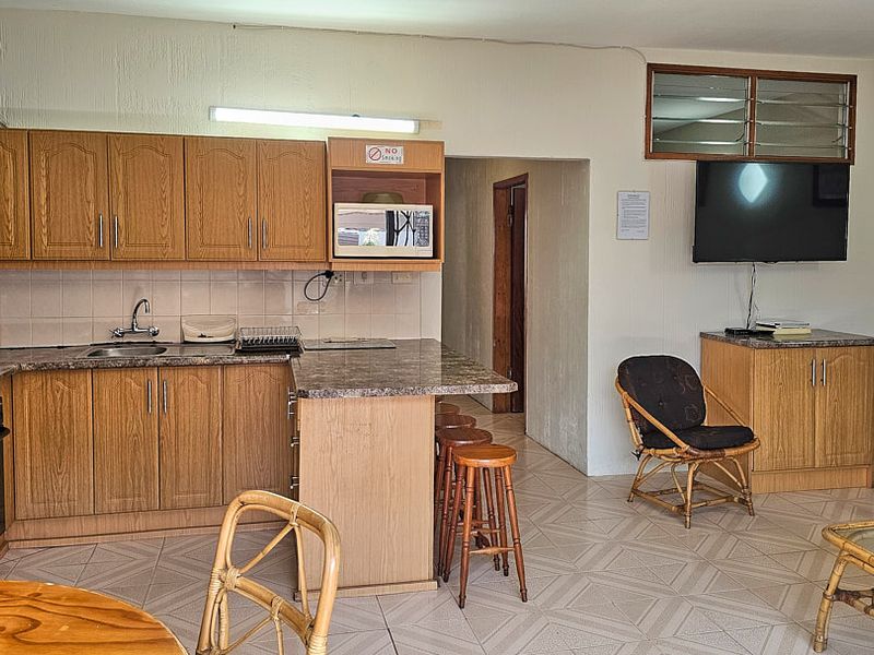 Open-plan kitchen and living area featuring wood-finish cabinetry, laminate countertops, built-in oven, and tiled flooring throughout.