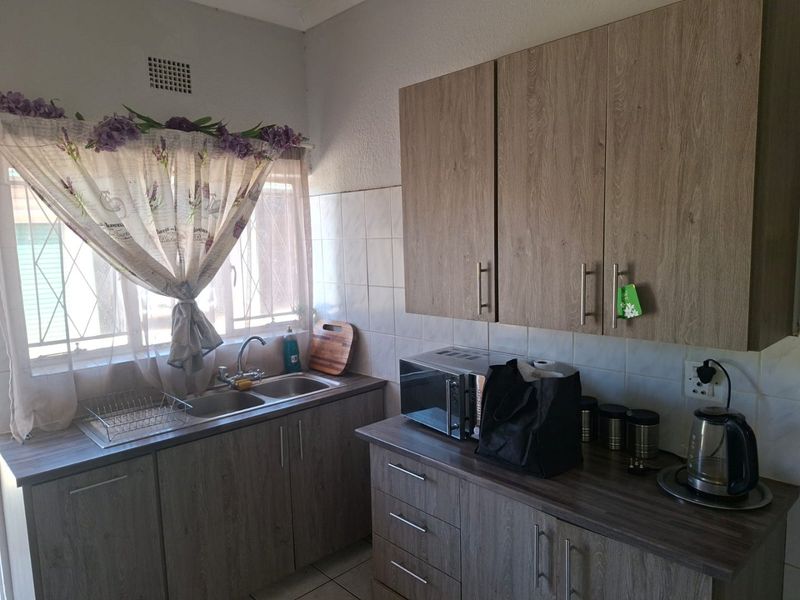 A functional kitchen featuring wood-look laminate cabinetry, durable countertops, a double basin sink, and a tiled backsplash with security bars on the window.