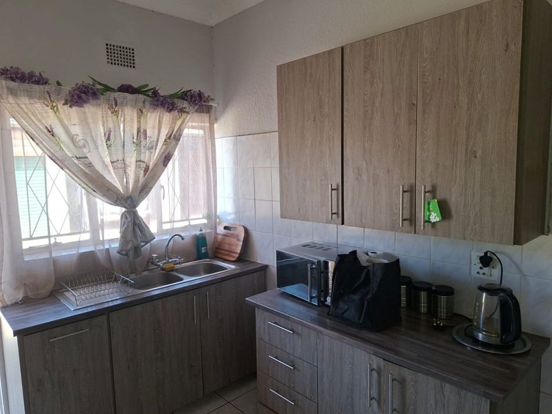 A functional kitchen featuring wood-look laminate cabinetry, double stainless steel sink, tiled splashbacks, and ample counter space for meal preparation.