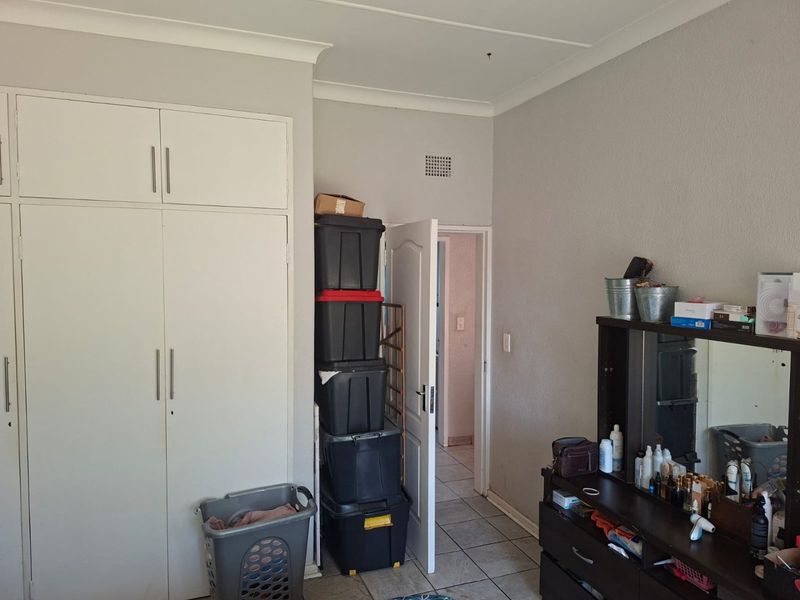 A bedroom featuring built-in cupboards, tiled flooring, and coved ceiling details, providing a functional space with direct access to an adjoining room.