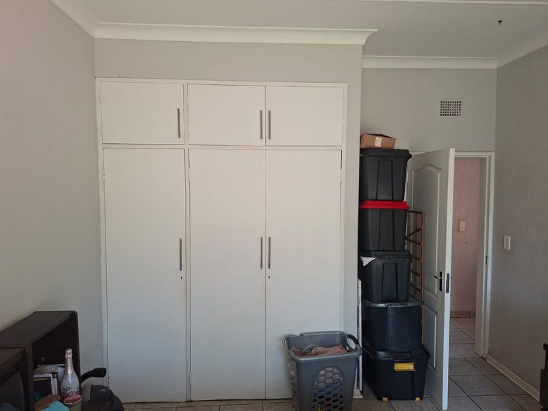 A bedroom featuring white built-in cupboards with modern handles, tiled flooring, and decorative ceiling coving.
