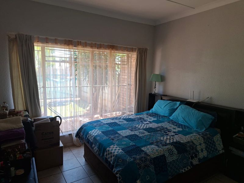 A bedroom featuring tiled flooring and a large sliding glass door with security gate, providing access to an outdoor area.