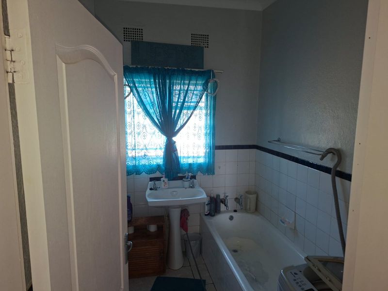 A functional bathroom featuring a pedestal basin, bathtub, and tiled splashback, requiring cosmetic updates to modernize the space.
