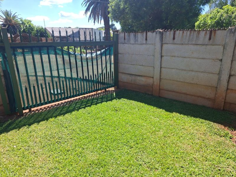A private rear garden area featuring a well-maintained lawn, enclosed by a precast concrete boundary wall and a metal security gate with spiked fencing.