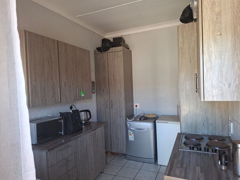 A functional kitchen featuring wood-look laminate cabinetry, dark countertops, an electric hob, and tiled flooring, offering a practical layout for daily use.