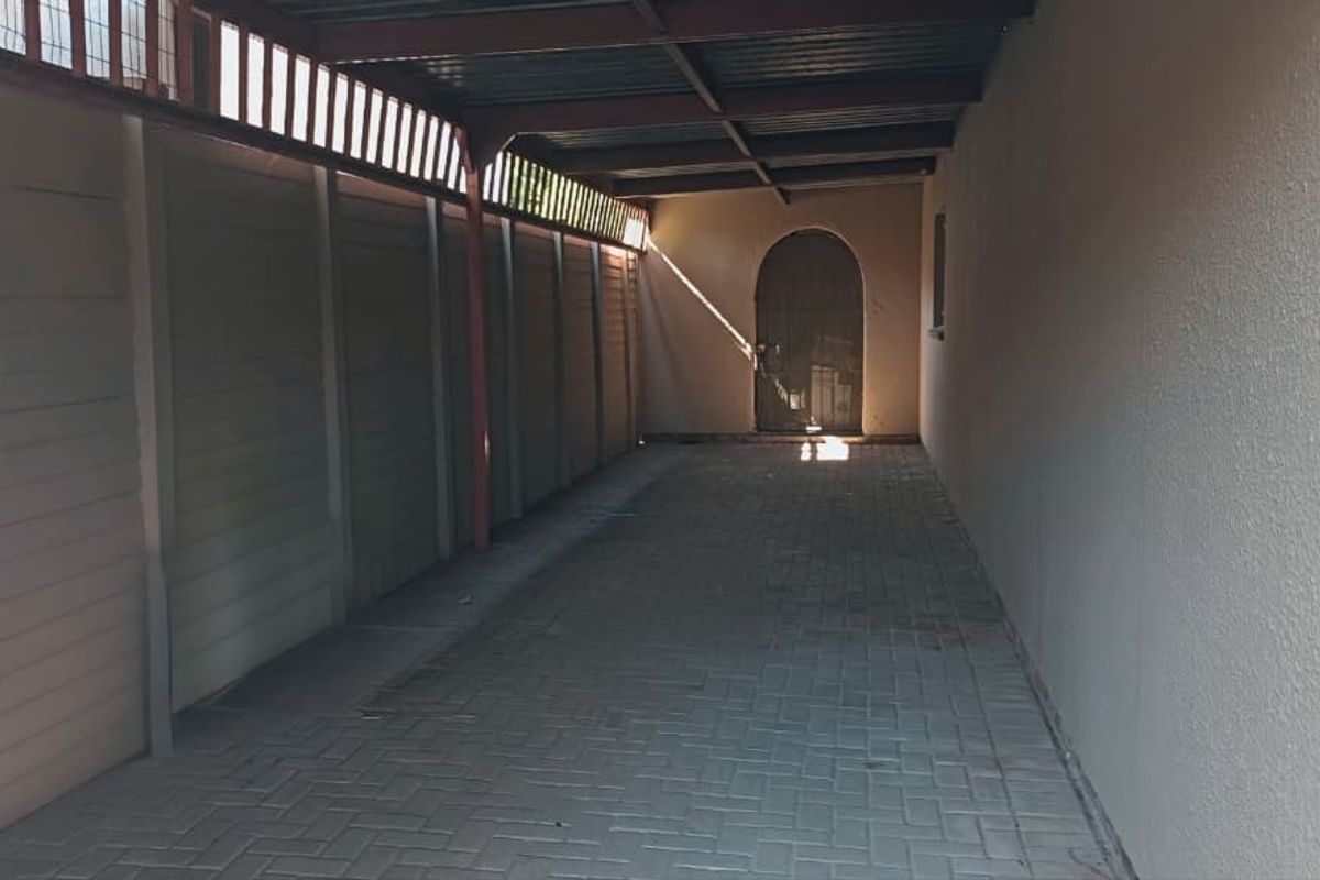 A covered side passage or carport area featuring paved flooring, a precast boundary wall, and an arched entrance door.
