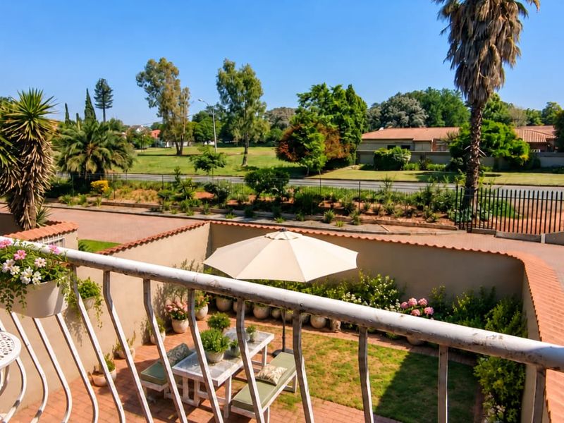 Elevated balcony overlooking a private courtyard garden and the surrounding neighbourhood, featuring a metal balustrade and brick paved flooring.