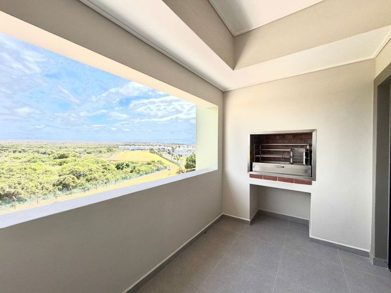 A modern covered balcony featuring a built-in braai, tiled flooring, and expansive views of the surrounding landscape.