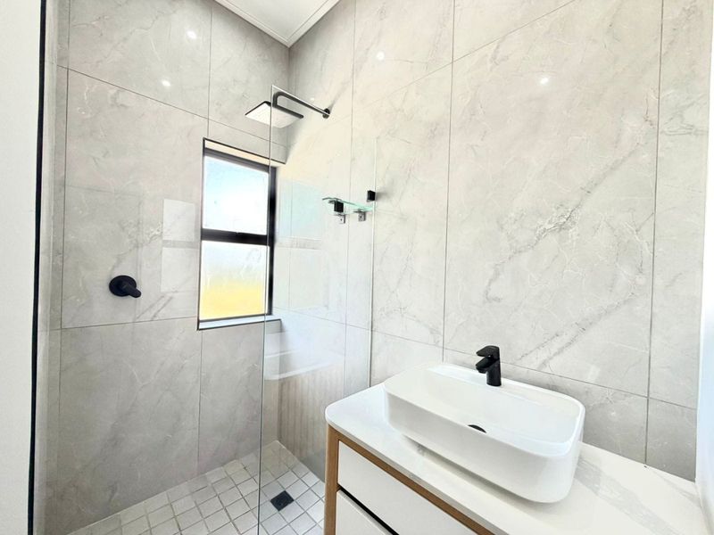 Modern bathroom featuring marble-look wall tiles, a glass shower enclosure with a rain shower head, and a contemporary vanity with a vessel sink.