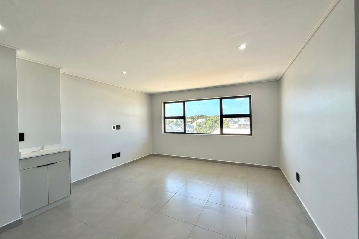 A bright, empty living area featuring neutral tiled flooring, recessed downlighting, and built-in cabinetry, offering a clean canvas for interior design.
