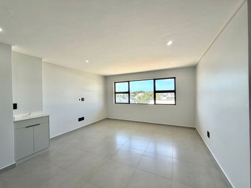 A bright, empty living area featuring neutral tiled flooring, recessed downlighting, and built-in cabinetry, offering a clean canvas for interior design.