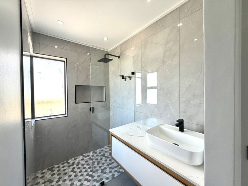 Modern bathroom featuring a walk-in shower with a recessed niche, floating vanity with a vessel sink, and contemporary grey marble-look wall tiles.