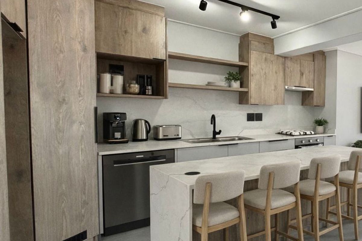 Modern kitchen featuring wood-grain cabinetry, stone countertops, a central island with breakfast bar seating, and integrated appliances.