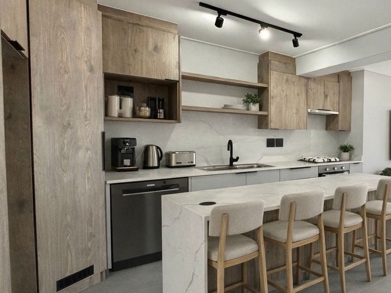 Modern kitchen featuring wood-grain cabinetry, stone countertops, a central island with breakfast bar seating, and integrated appliances.