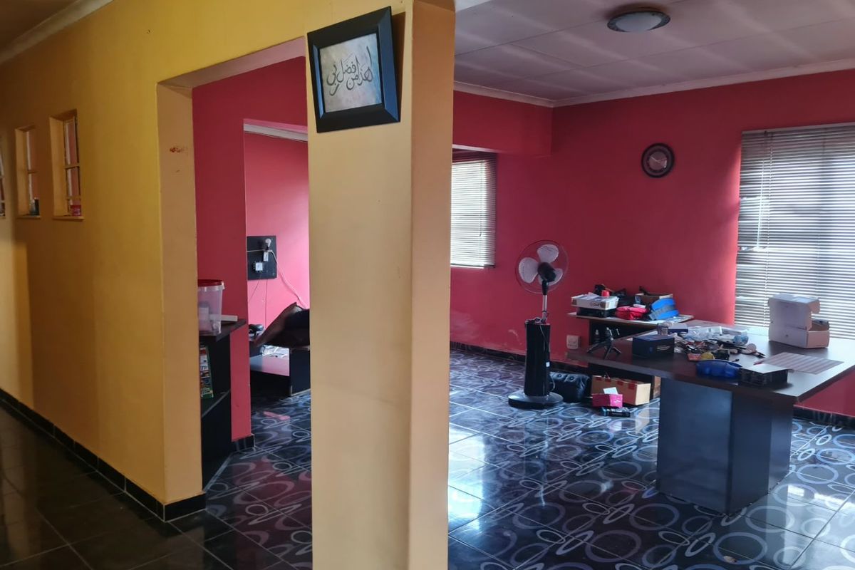 An open-plan living area featuring dark patterned floor tiles, red and yellow wall finishes, and window blinds.