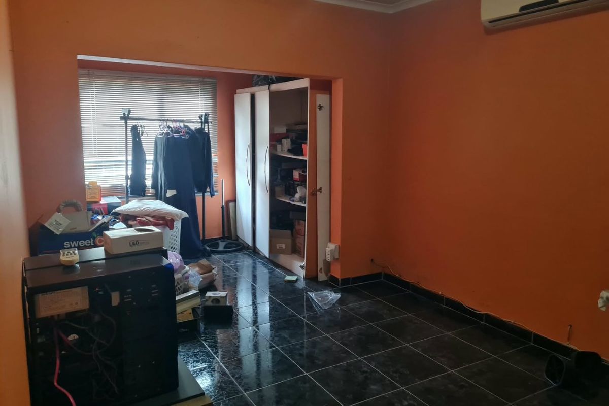 A bedroom featuring dark tiled flooring, a built-in wardrobe, and a wall-mounted air conditioning unit, currently used as a storage and utility space.