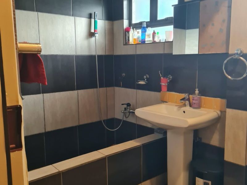 A functional bathroom featuring a pedestal basin, built-in bathtub with shower mixer, and contrasting black and grey wall tiling.